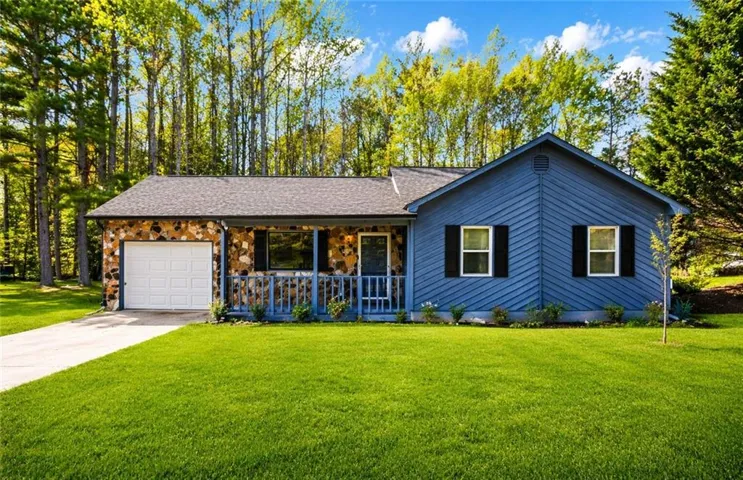 View of front of property with covered porch, a front lawn, concrete driveway, an attached garage, and stone siding