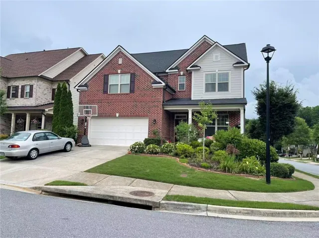 Brick and siding exterior featuring a covered front porch, an attached garage, a paved driveway, a landscaped front yard, and a streetlamp