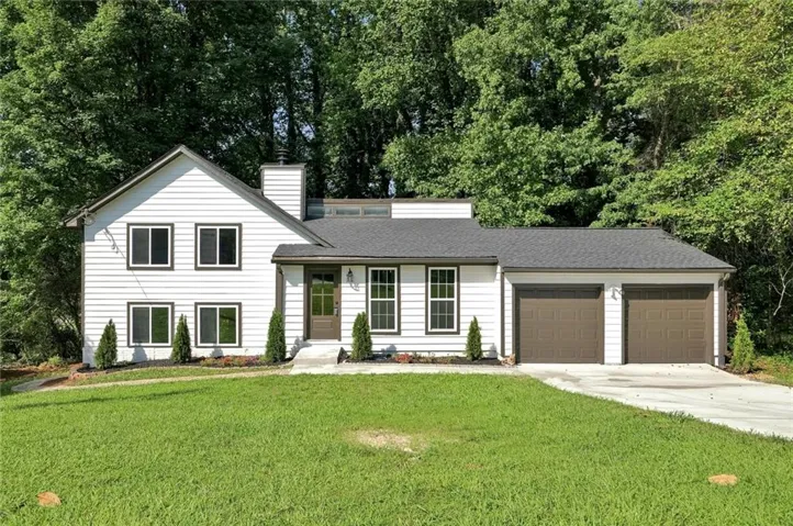 White siding exterior with a dark shingle roof, featuring a two-car garage with brown doors, a concrete driveway, and a front entry with a brown door