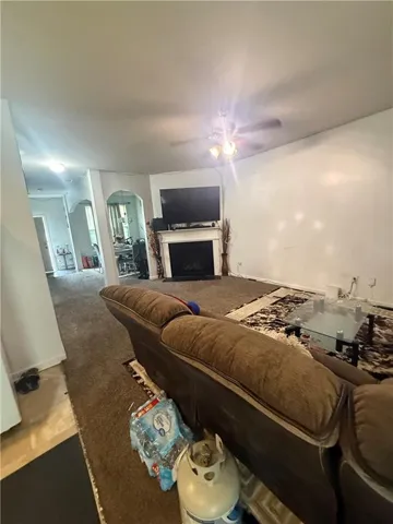 Living area featuring a corner fireplace with a white mantel, ceiling fan, and carpeted flooring
