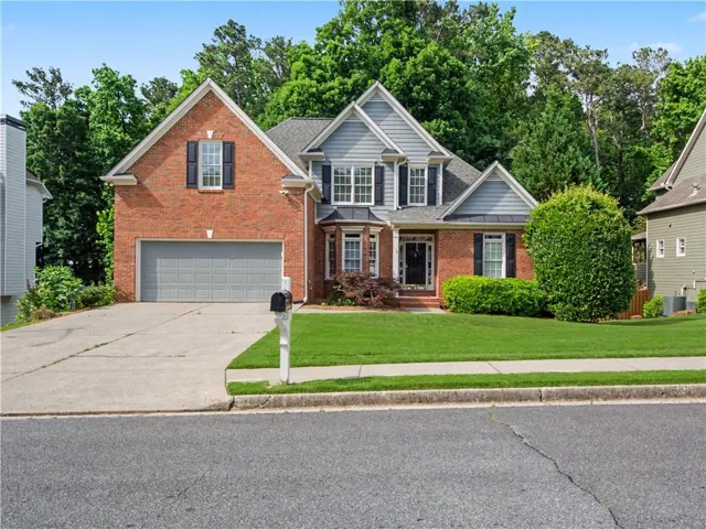 Traditional-style home featuring a brick and siding exterior, an attached garage, a bay window, and a manicured front lawn with established landscaping