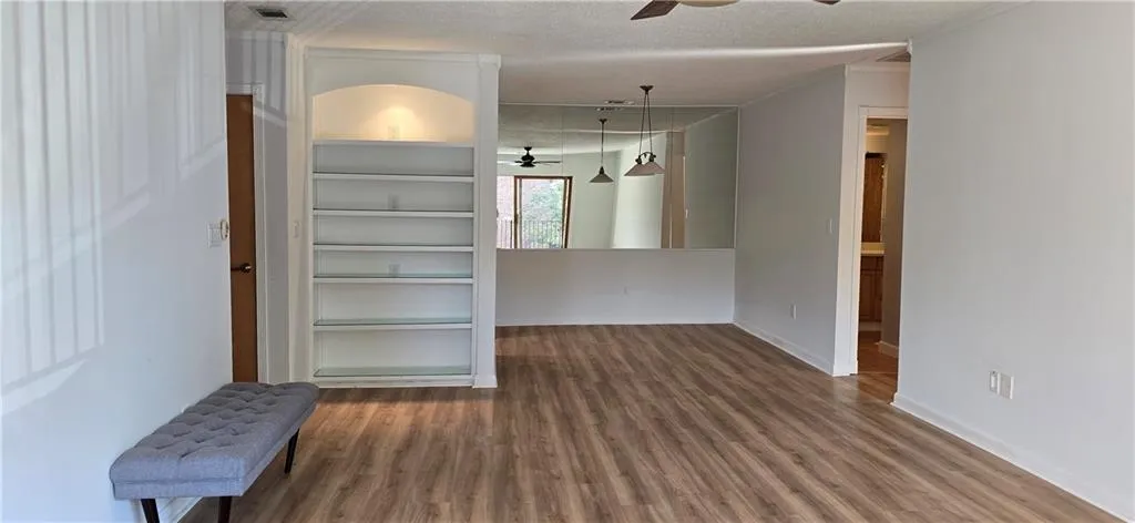 Unfurnished room with wood-type flooring, ceiling fan, built in features, and a textured ceiling