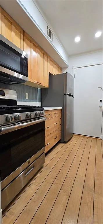 Kitchen featuring stove, light brown cabinetry, stainless steel refrigerator, and light hardwood / wood-style flooring