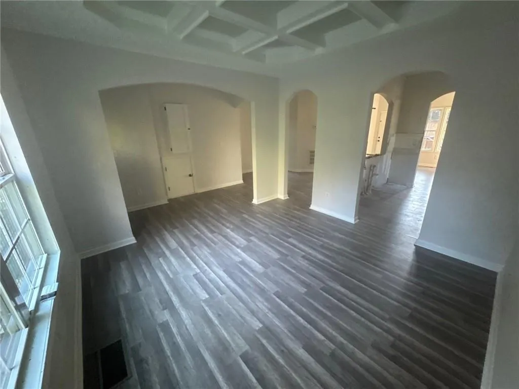 Unfurnished room with coffered ceiling, beam ceiling, dark wood-style floors, and arched walkways
