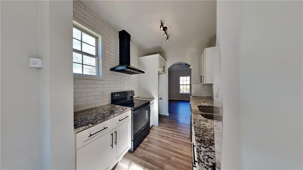 Kitchen with decorative backsplash, stone counters, black / electric stove, and wall chimney range hood