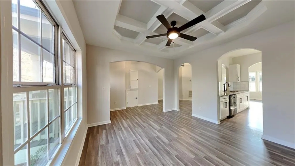 Empty room featuring arched walkways, wood finished floors, a sink, beamed ceiling, and coffered ceiling