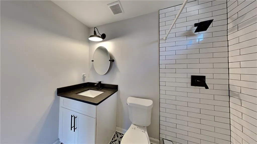 Bathroom featuring visible vents, vanity, toilet, baseboards, and a tile shower