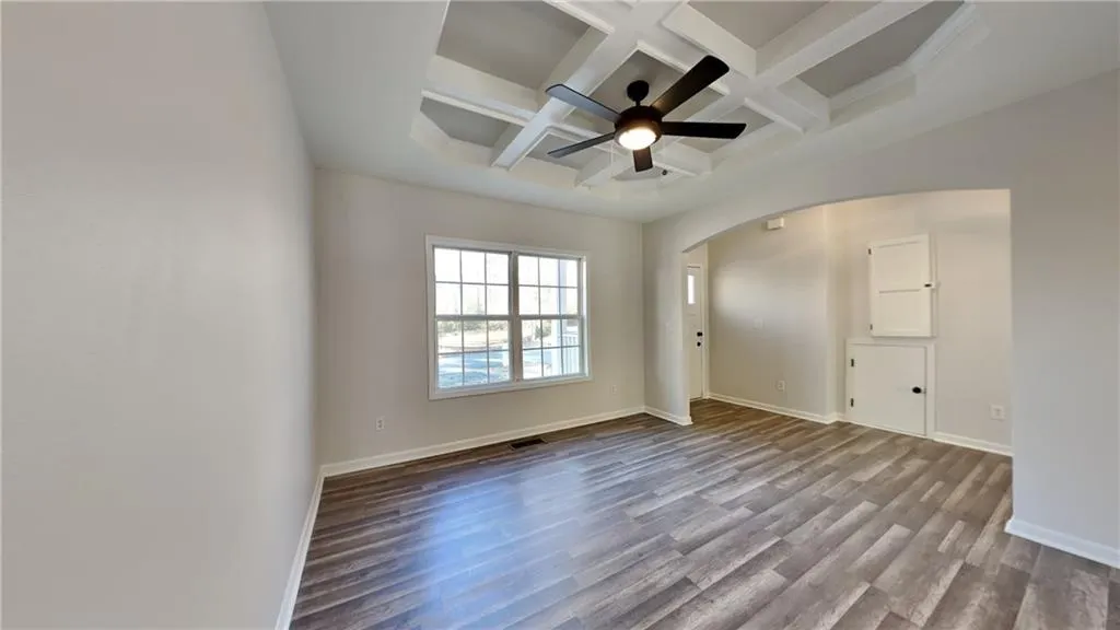 Empty room with arched walkways, coffered ceiling, beam ceiling, and dark wood-style floors