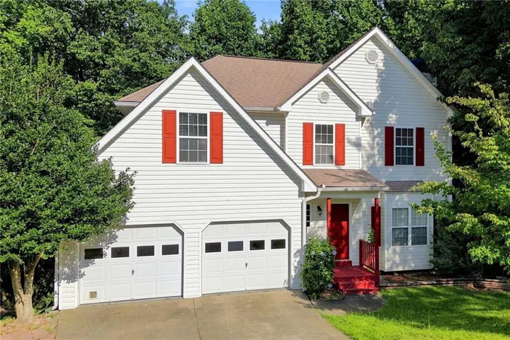 Two-story residence featuring white siding, a contrasting red entry door, matching red shutters, and a two-car garage