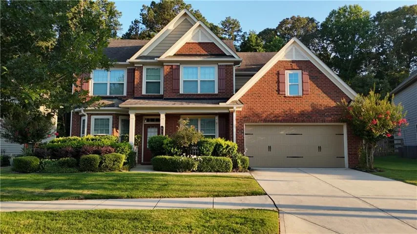 View of front of home featuring a front lawn, driveway, brick siding, covered porch, and roof with shingles