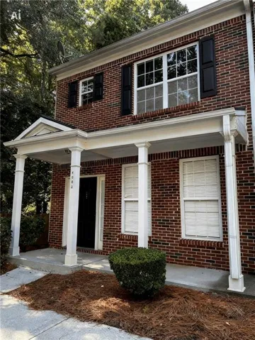 Brick exterior featuring a covered porch with white columns, multi-pane windows with dark shutters, and a dark front door