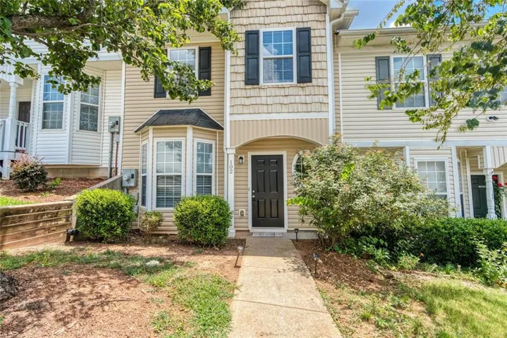 Multi-level townhouse exterior featuring light-toned siding, a prominent bay window, dark shutters, and a covered entry