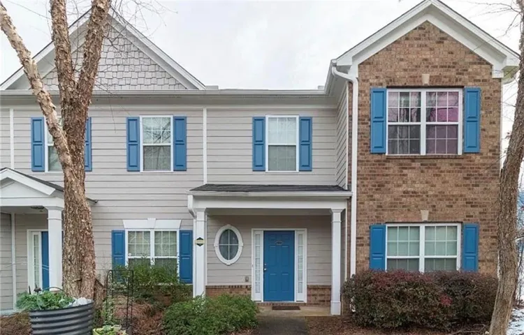 Charming two-story colonial featuring blue vinyl shutters, brick and siding exterior, arched entryway with oval transom window, and mature landscaping with established trees flanking the front elevation