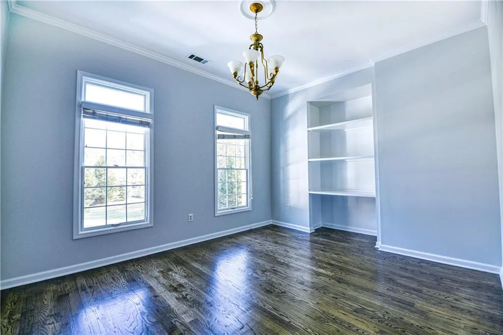 Unfurnished room featuring dark wood-style flooring, visible vents, crown molding, baseboards, and a notable chandelier