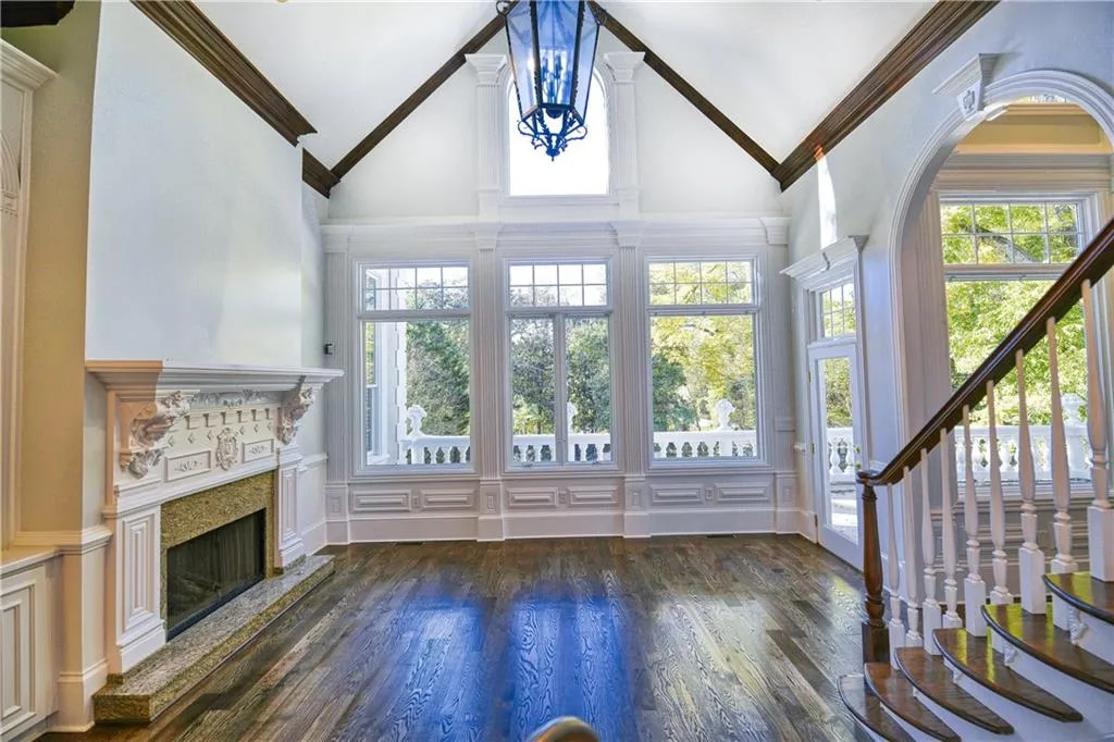 Unfurnished living room with dark wood-style flooring, high vaulted ceiling, a high end fireplace, ornamental molding, and stairway