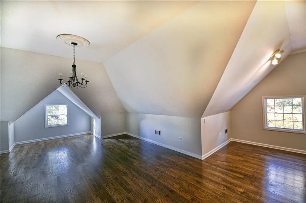 Additional living space with dark wood-style floors, visible vents, baseboards, and an inviting chandelier