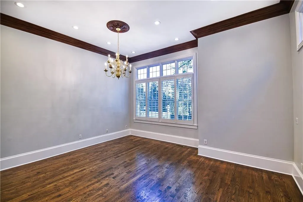 Empty room with baseboards, dark wood-style flooring, an inviting chandelier, and crown molding