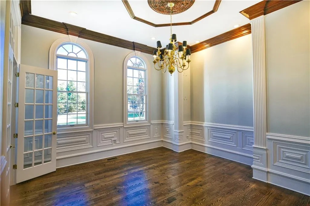 Unfurnished dining area featuring crown molding, wood finished floors, an inviting chandelier, and wainscoting
