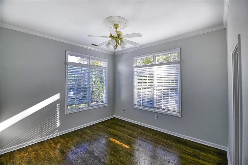 Empty room with baseboards, crown molding, ceiling fan, and dark wood-style flooring