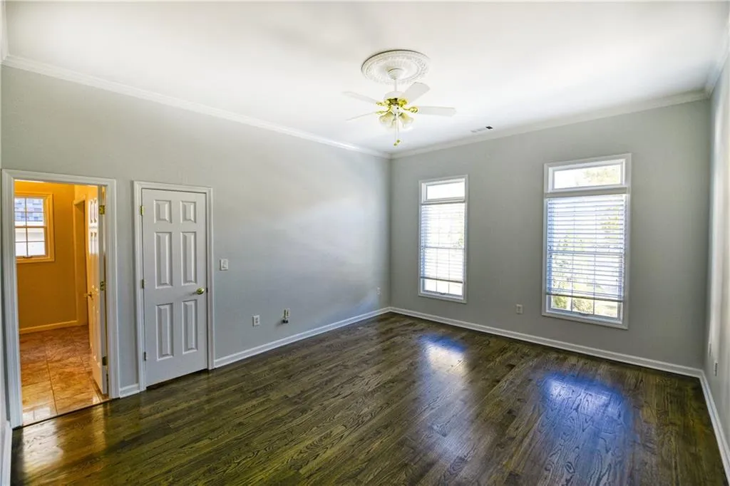 Spare room featuring dark wood finished floors, baseboards, visible vents, ceiling fan, and ornamental molding