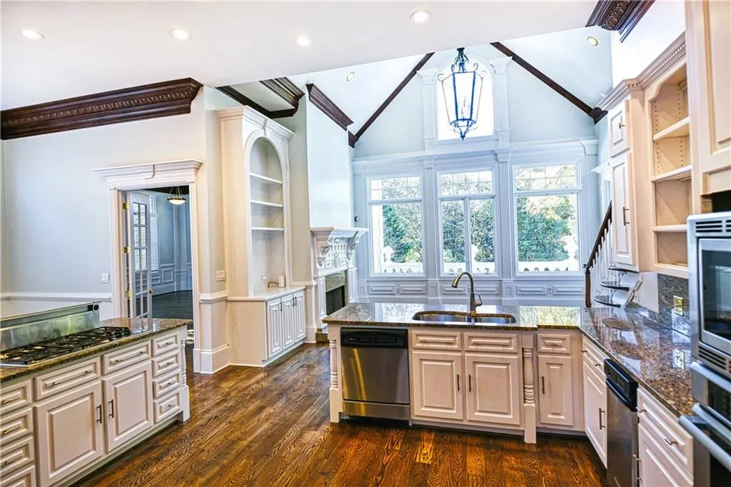 Kitchen with dark wood-style flooring, appliances with stainless steel finishes, lofted ceiling, dark stone countertops, and a sink