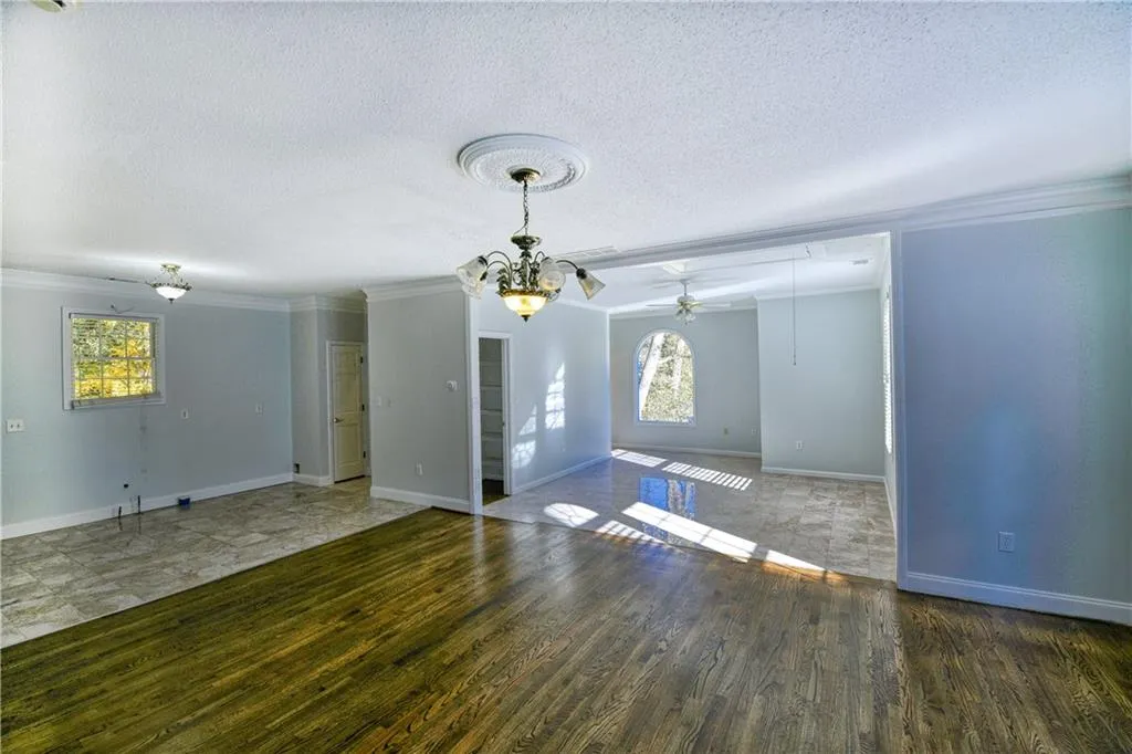 Unfurnished room featuring ceiling fan with notable chandelier, wood finished floors, ornamental molding, and a textured ceiling