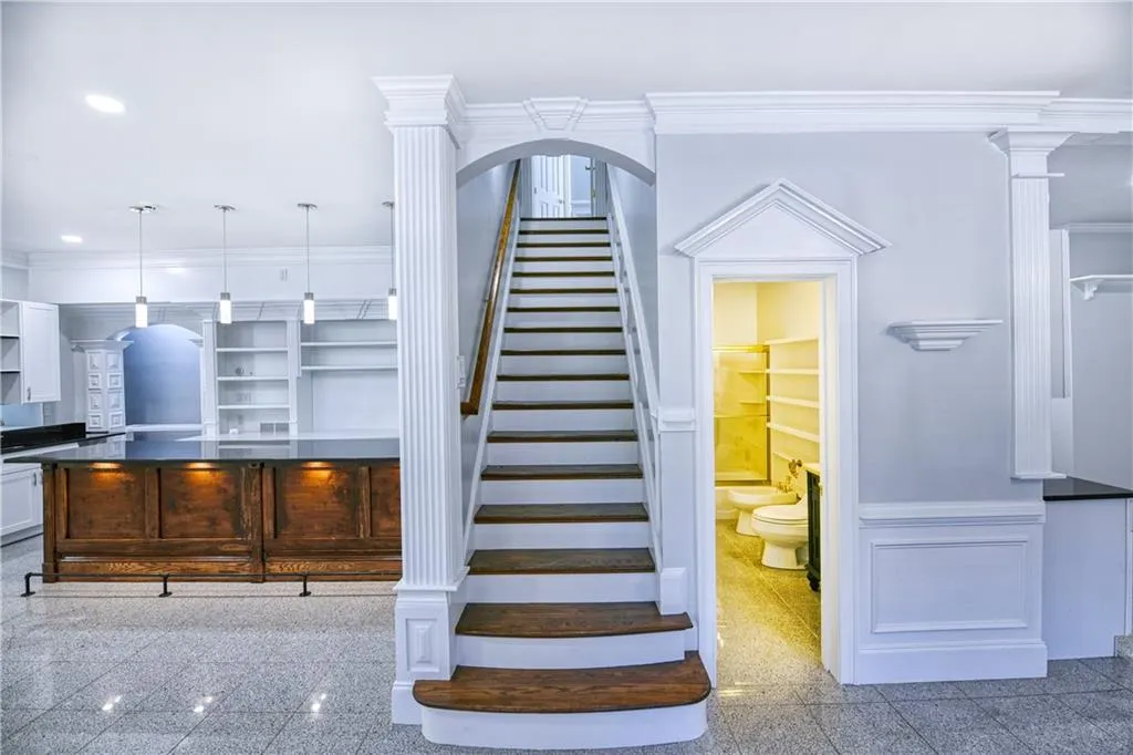 Staircase with a decorative wall, ornamental molding, granite finish floor, and wainscoting