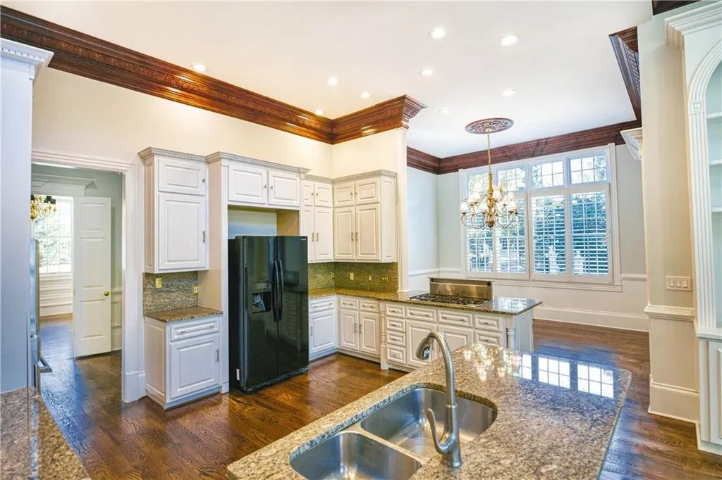 Kitchen featuring a sink, black fridge with ice dispenser, light stone counters, and a chandelier