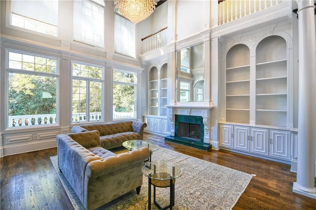 Living area with dark wood-style flooring, a chandelier, built in shelves, a towering ceiling, and a fireplace