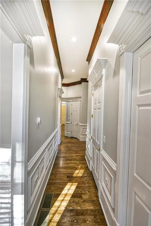 Hallway featuring crown molding, recessed lighting, dark wood-style floors, a decorative wall, and wainscoting