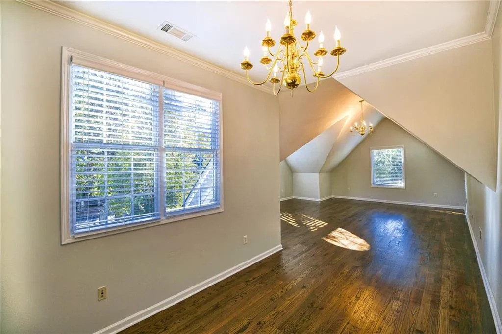 Bonus room featuring lofted ceiling, an inviting chandelier, baseboards, visible vents, and hardwood / wood-style floors
