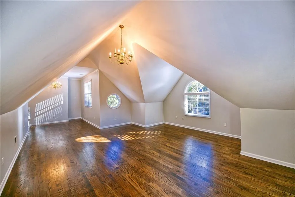 Additional living space with baseboards, wood finished floors, a notable chandelier, and plenty of natural light
