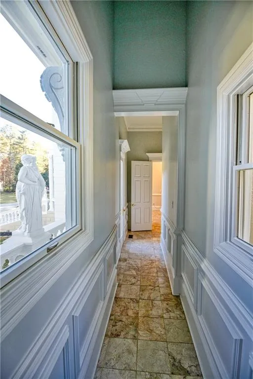 Hallway with a decorative wall, wainscoting, and stone finish flooring