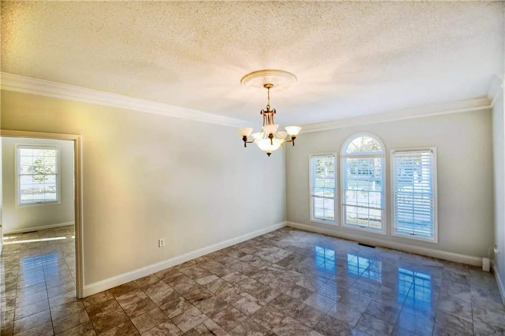 Spare room featuring baseboards, a notable chandelier, crown molding, and a textured ceiling