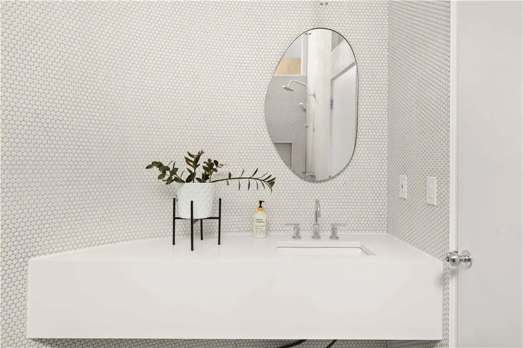 Wall-mounted floating vanity with integrated rectangular sink and polished metal widespread faucet, complemented by an oval wall mirror and full-height penny tile wall surfacing