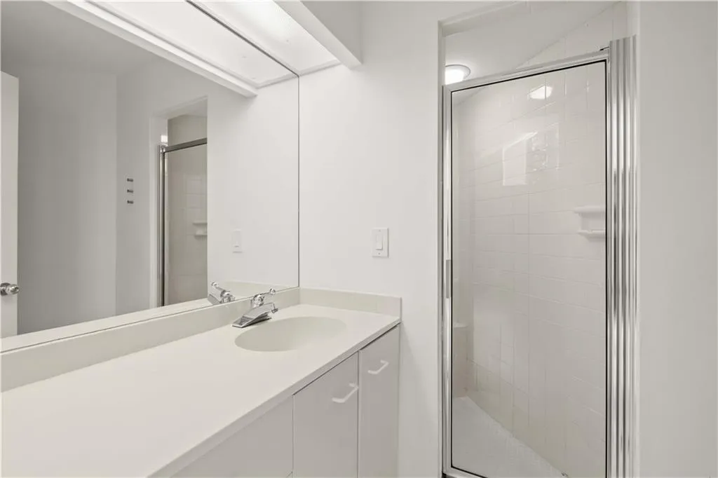 Bathroom vanity with an integrated sink, solid surface countertop, full-width mirror, and a shower enclosure featuring tiled walls and a glass door