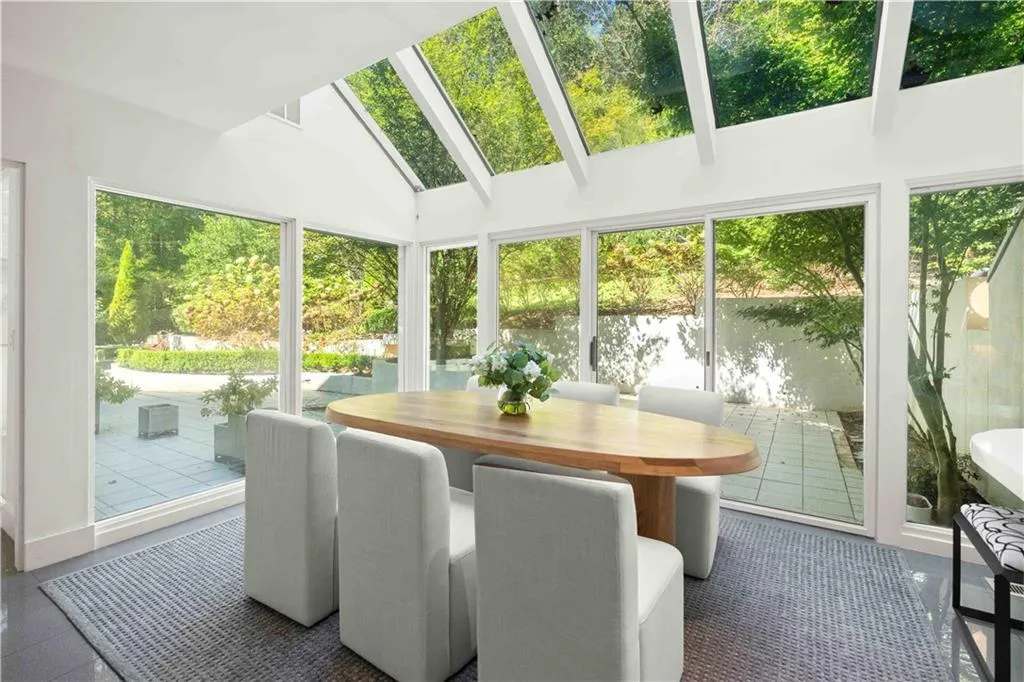 Sunroom featuring vaulted ceilings with integrated skylights, expansive glass wall panels, and sliding glass door access to a stone-paved patio