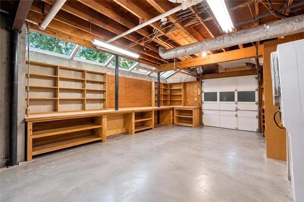 Workshop area featuring concrete flooring, extensive built-in wood shelving, an expansive workbench, natural light via overhead skylights, and fluorescent strip lighting