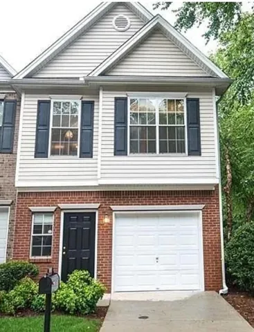Brick and siding exterior featuring a prominent gable, white paneled garage door, black entry door, and dark louvered shutters