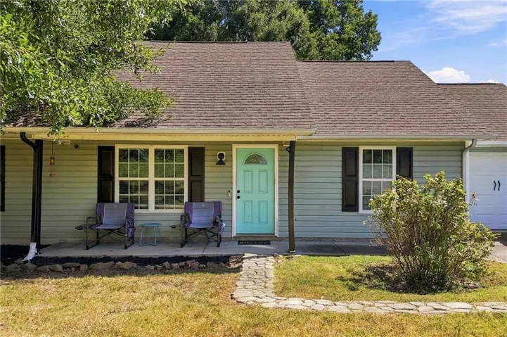 Light blue siding exterior featuring a covered porch, a bright turquoise entry door, a stone-finish walkway, and an attached garage with a double door