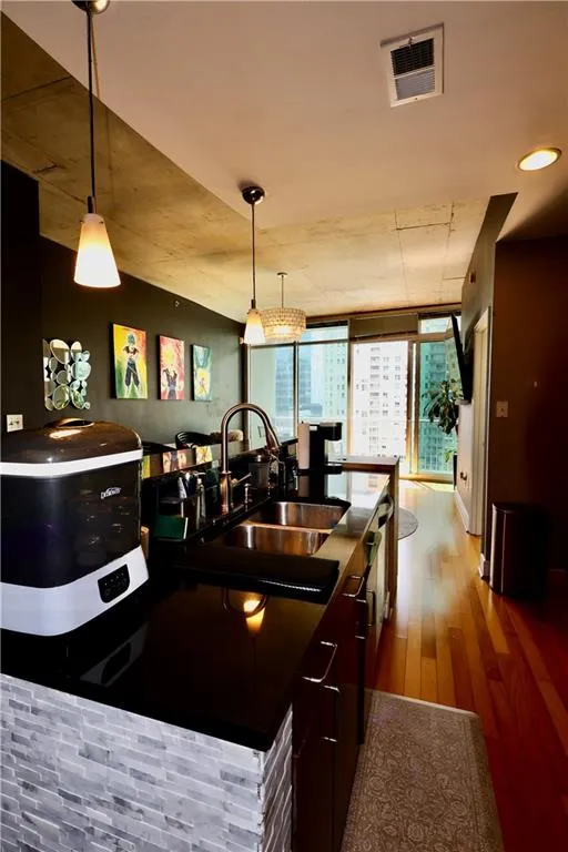 Kitchen featuring light wood-type flooring, pendant lighting, a wall of windows, modern cabinets, and dark countertops