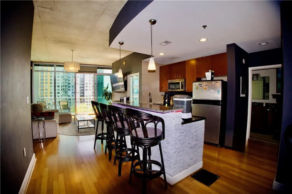 Kitchen featuring appliances with stainless steel finishes, expansive windows, pendant lighting, dark wood-style floors, and brown cabinets