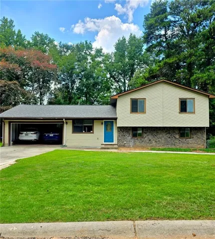 Split-level residence featuring a two-car garage, stone and siding exterior, and a bright blue front door