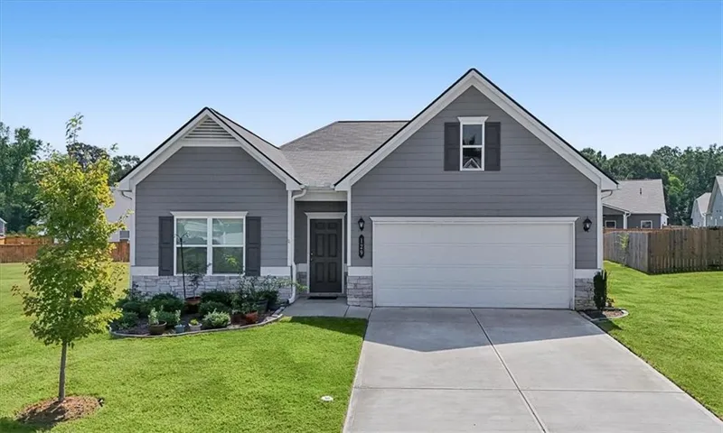 Single-story residence featuring grey siding, stone veneer accents, an attached garage, a paved driveway, and manicured landscaping