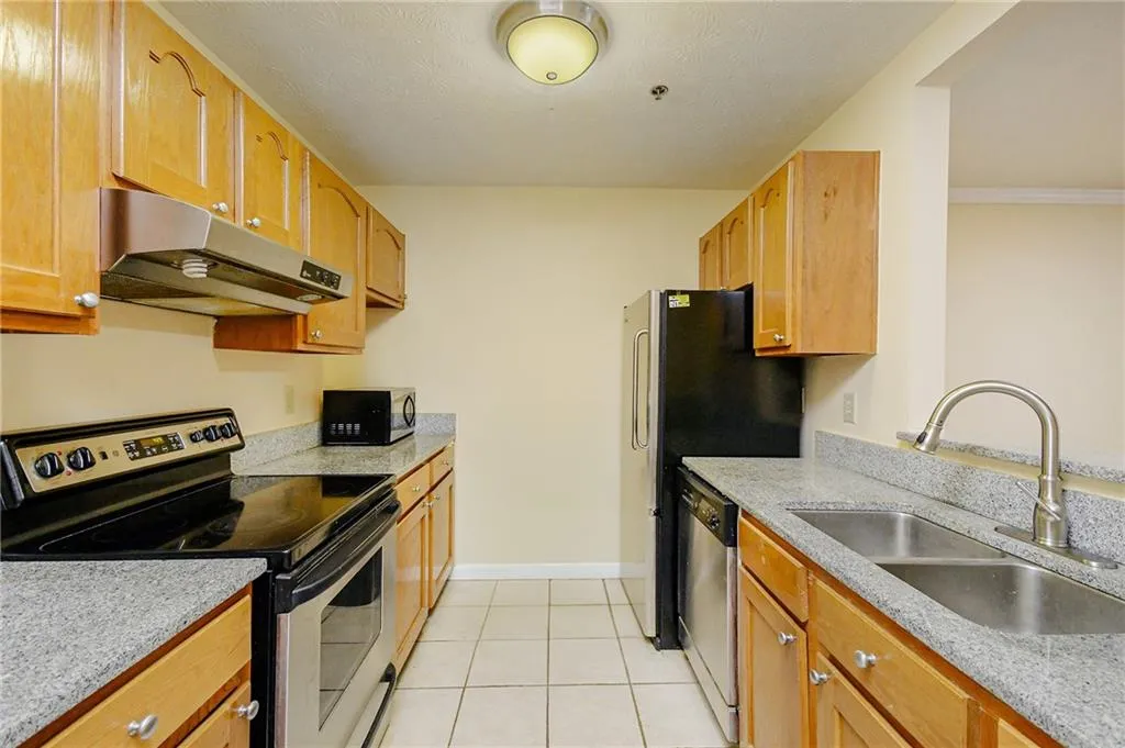 Kitchen with baseboards, under cabinet range hood, appliances with stainless steel finishes, light tile patterned flooring, and a sink