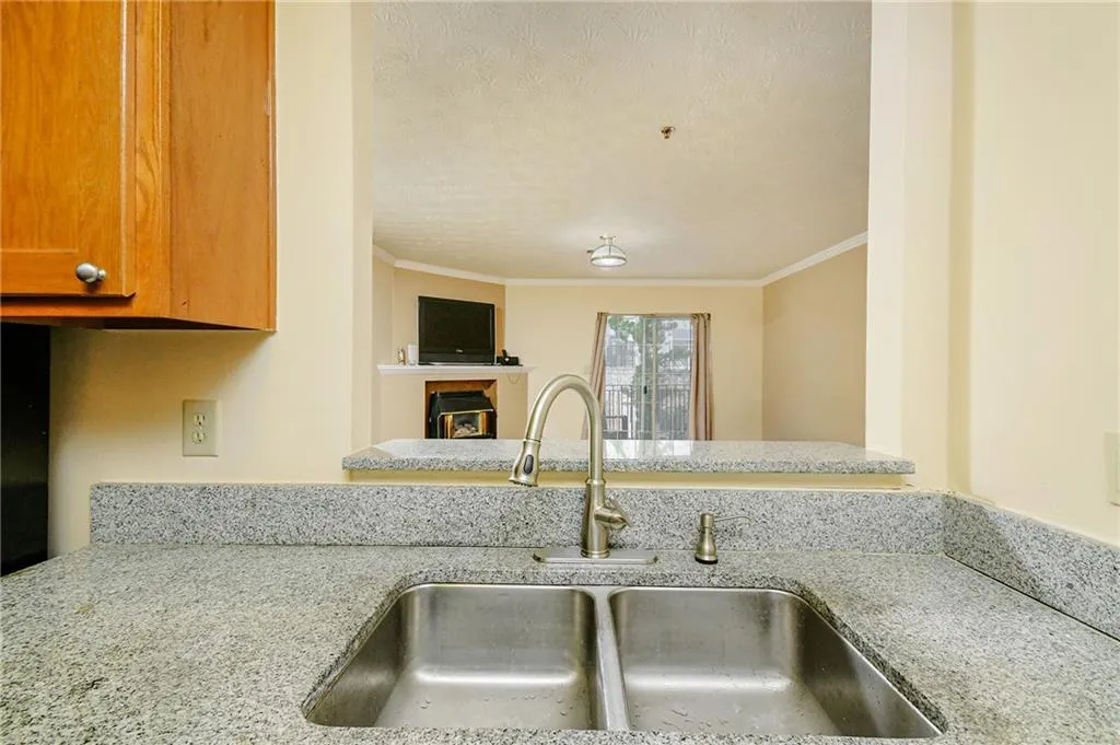 Kitchen featuring ornamental molding, a sink, a textured ceiling, light stone countertops, and a tile fireplace
