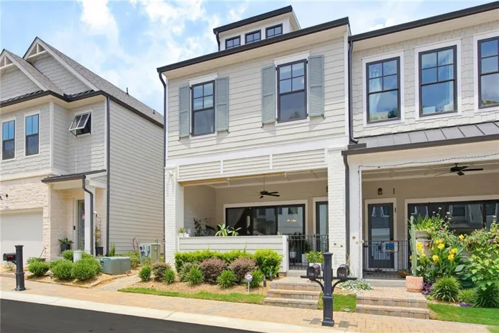 Modern townhome exterior featuring light-colored siding, black-framed windows, a covered porch with a ceiling fan, and a dormer