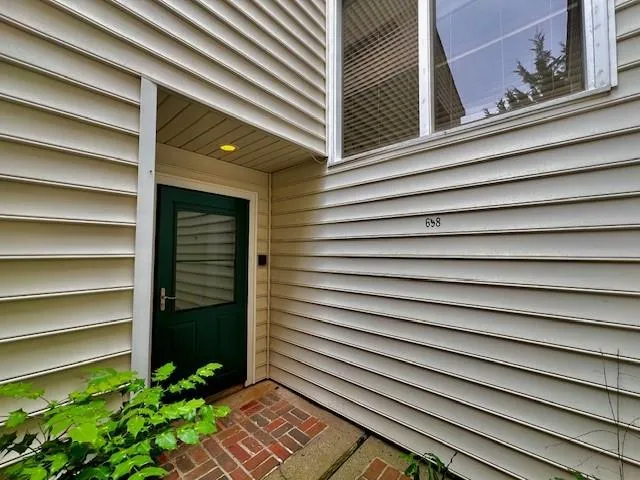 Entryway with a dark green door, brick paving, and white siding
