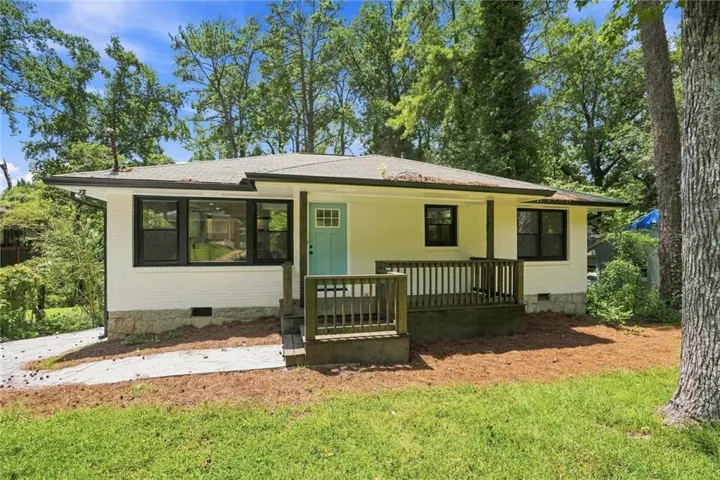 White brick exterior with black-framed windows, a light blue front door, and a covered front porch featuring wood railing