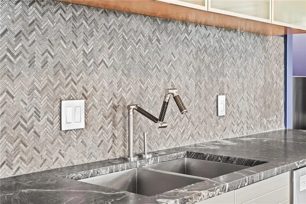 Beautiful herringbone contemporary tile accents the stone countertop and modern faucet